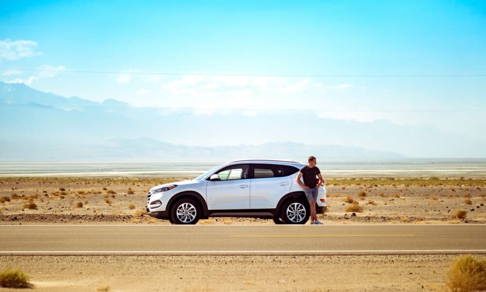 man standing beside white SUV near concrete road under blue sky at daytime