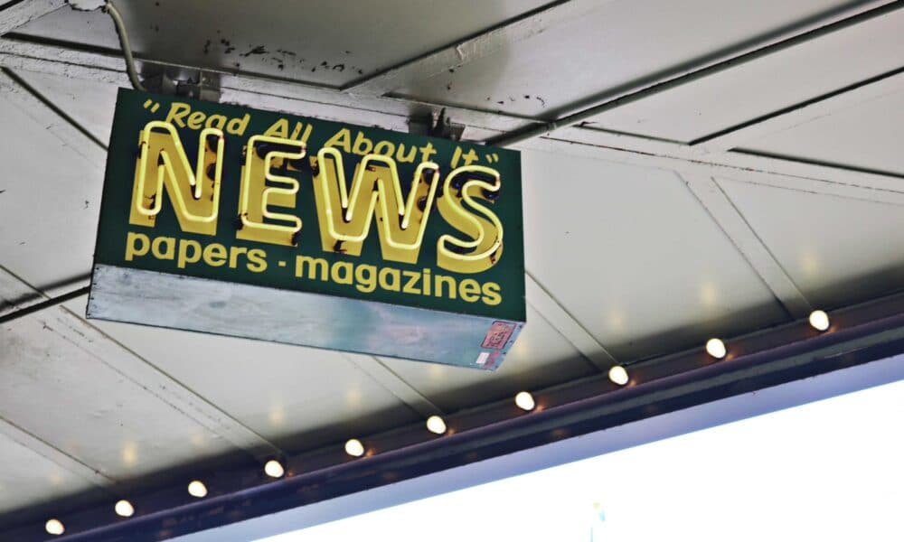 From below of illuminated signboard with news papers magazines inscriptions hanging on metal ceiling on street