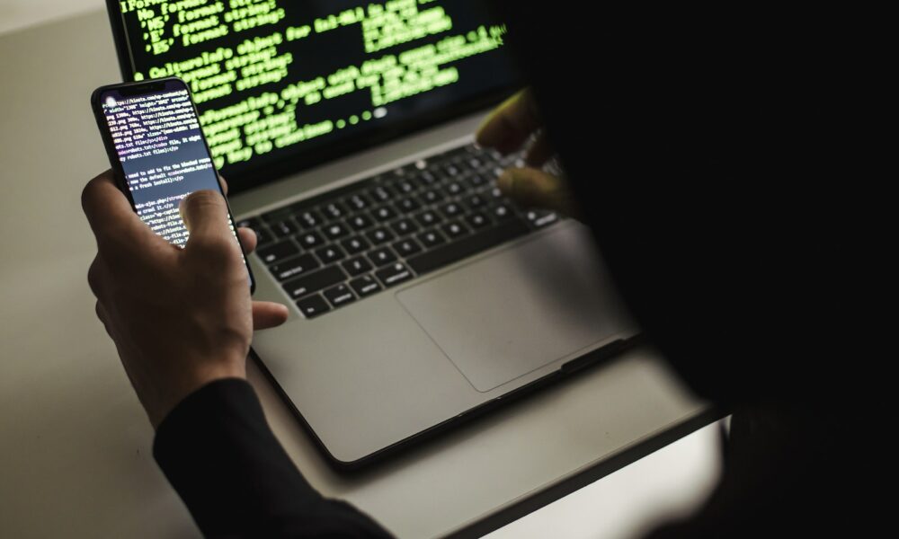 Crop unrecognizable developer using laptop and smartphone