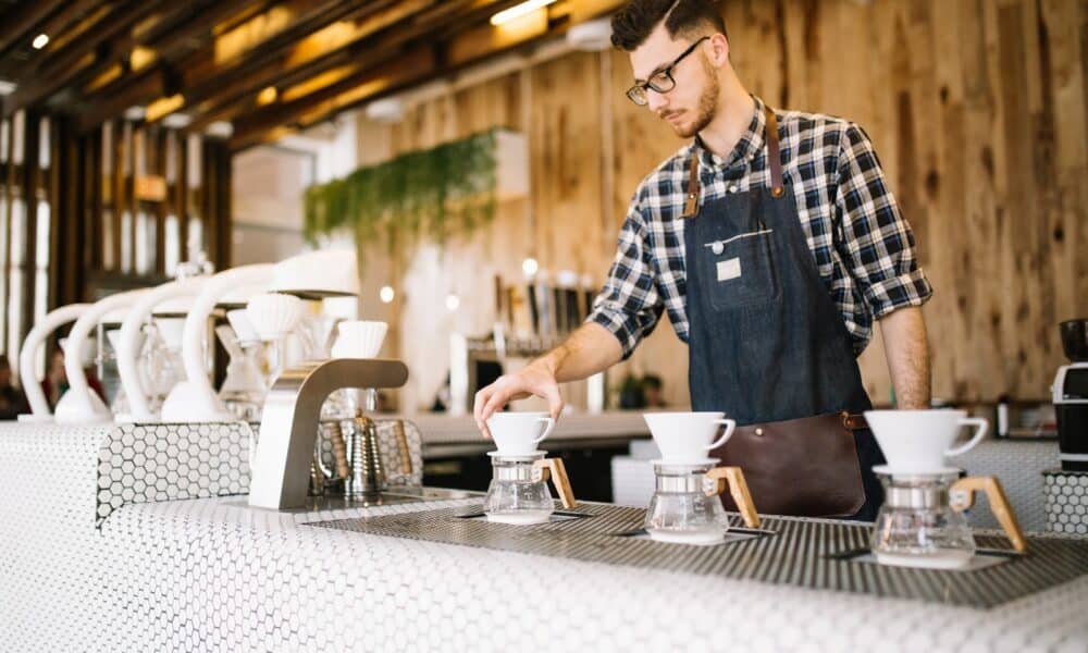 man in blue and white plaid button up shirt standing in front of table with mugs