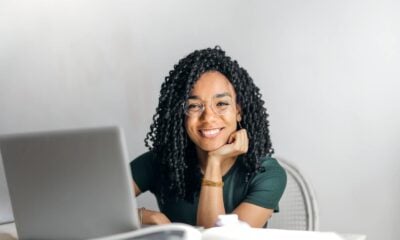 Happy ethnic woman sitting at table with laptop