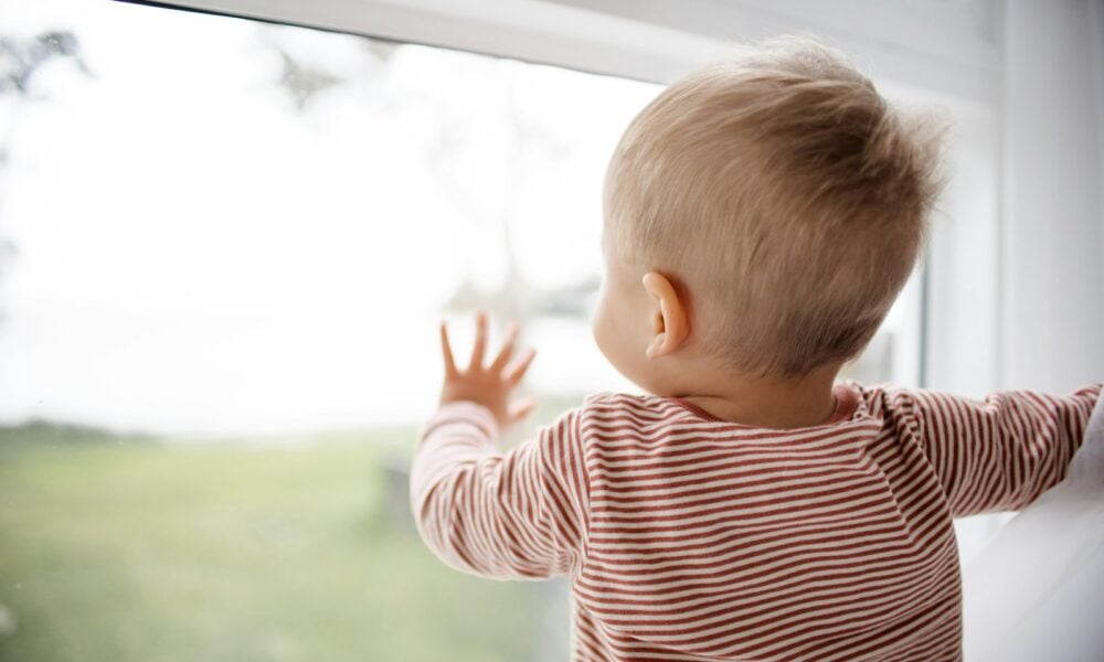 child in red and white striped shirt looking out the window