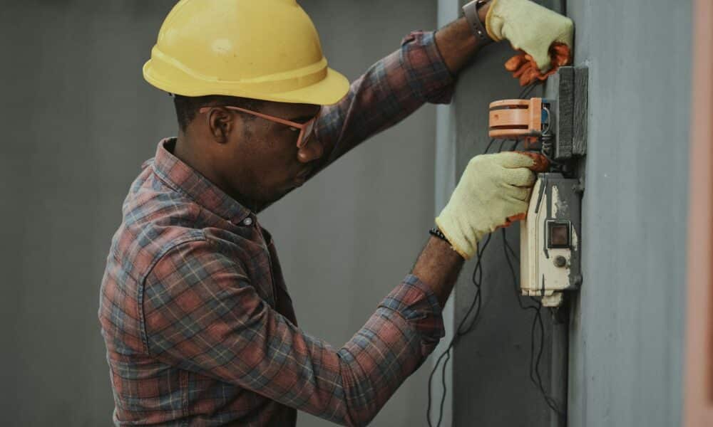 man in brown and white plaid dress shirt and yellow hard hat holding black and orange