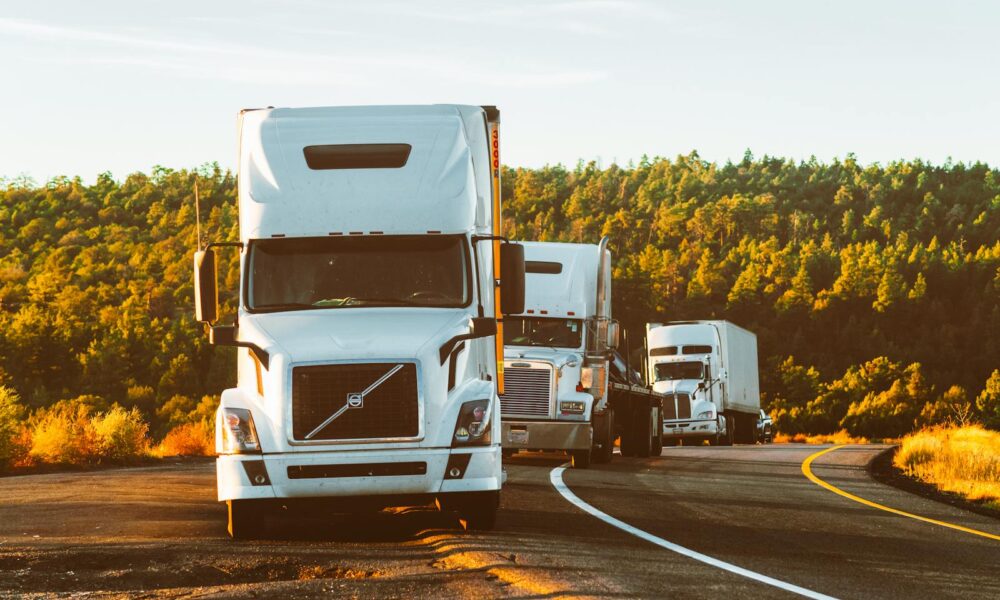 Three semi trucks driving on a highway through a forested landscape in Arizona.