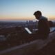man sitting on concrete brick with opened laptop on his lap