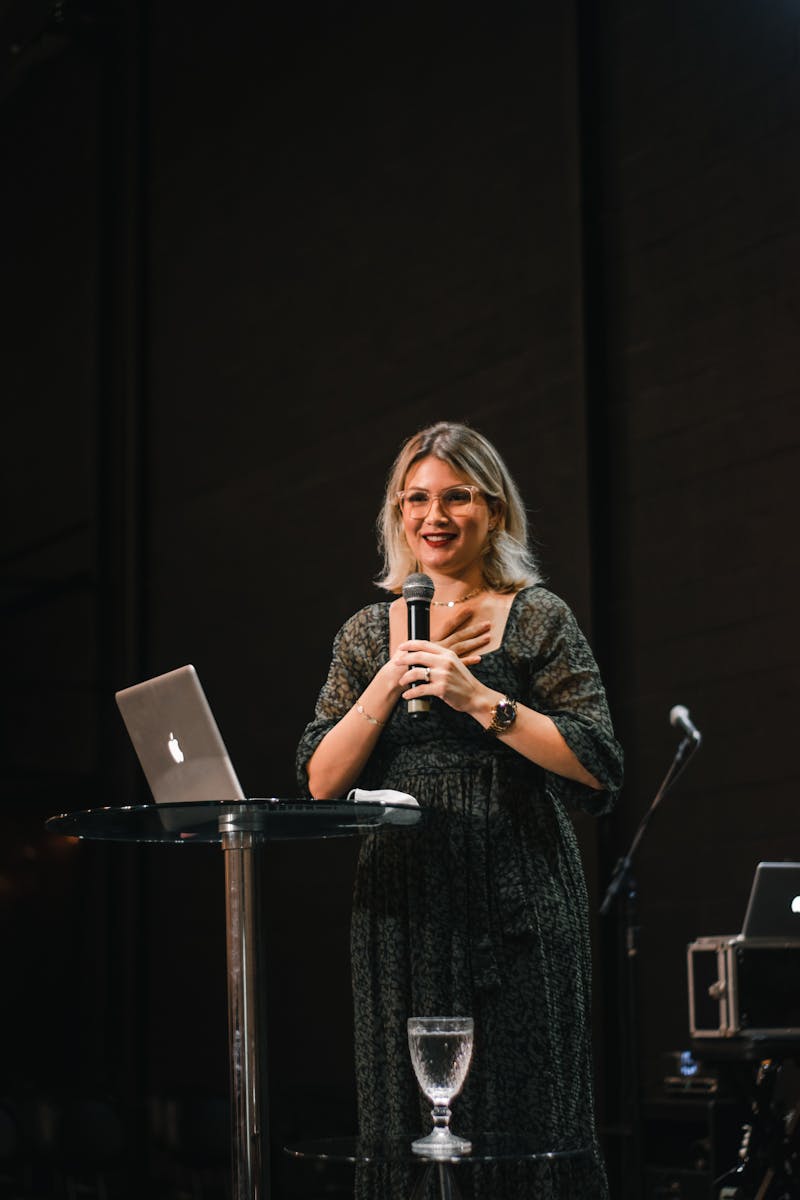 Where can I book an AI keynote speaker? 16 A woman giving a presentation on stage with a microphone and laptop.