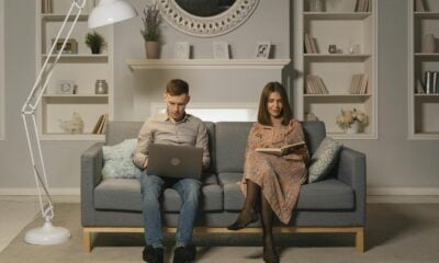A couple relaxing in a modern living room, reading and using a laptop on the couch.