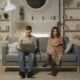 A couple relaxing in a modern living room, reading and using a laptop on the couch.