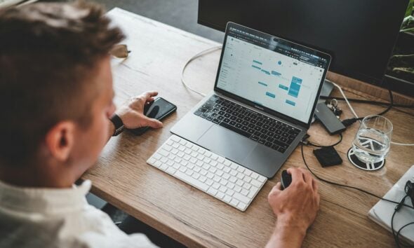 man holding mouse and iPhone while using Macbook Pro