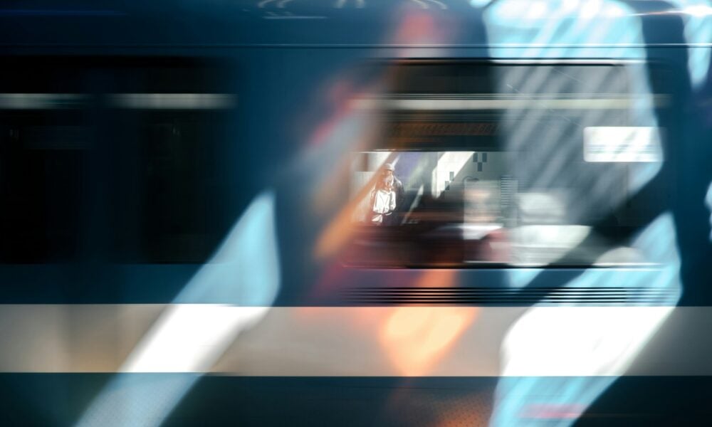 A blue train car blurring past briefly framing a person waiting