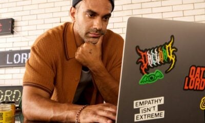 Man wearing a beanie and shirt works on a laptop.