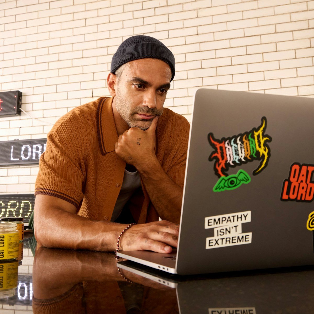 Man wearing a beanie and shirt works on a laptop.