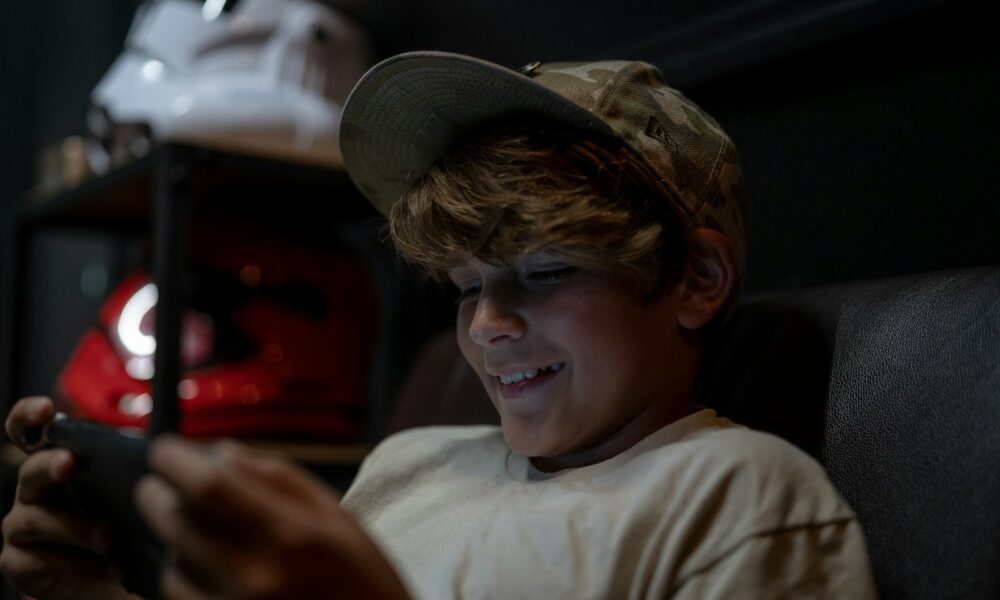 a young boy sitting in a chair looking at a cell phone