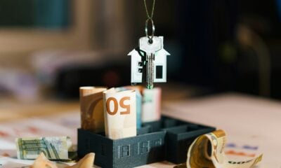 A house hanging from a string on top of a pile of money