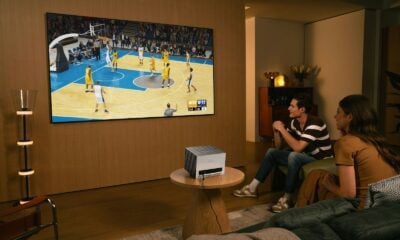 People watch a basketball game on a large screen.