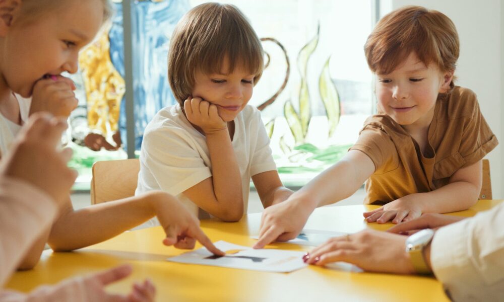 Young children engaging in fun learning activities at a yellow table in a classroom setting.