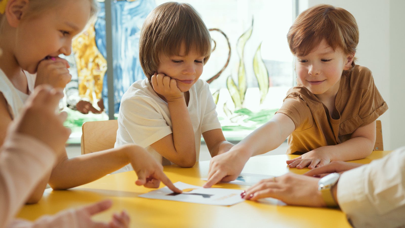 Do Smaller Class Sizes Always Mean Better Learning? 16 Young children engaging in fun learning activities at a yellow table in a classroom setting.