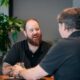 two men sitting at a table talking to each other