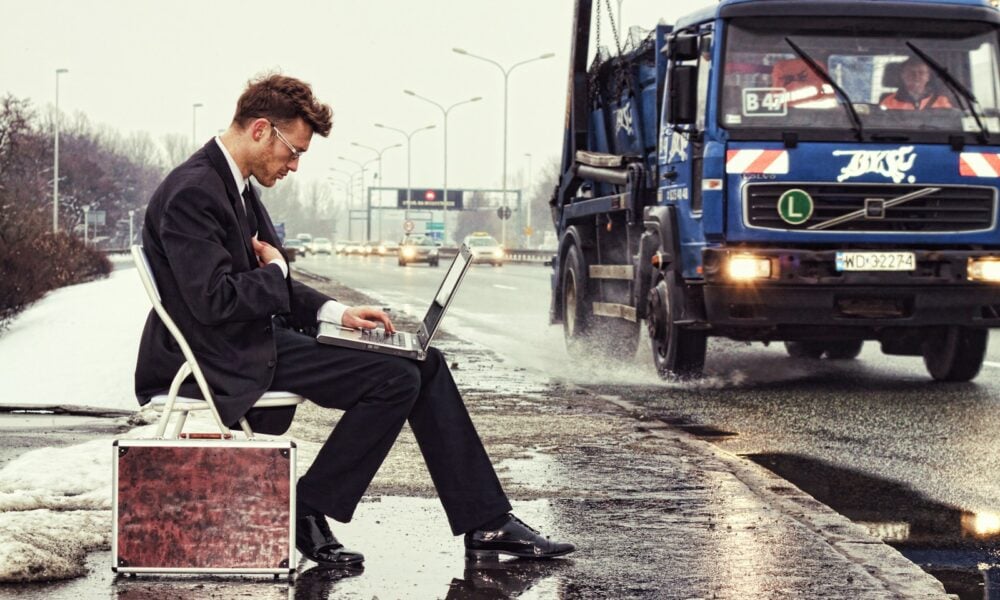 a man sitting on a suitcase on the side of the road