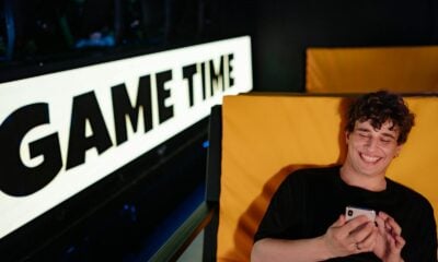 Smiling young man gaming on smartphone in a cozy indoor setting with 'Game Time' sign.