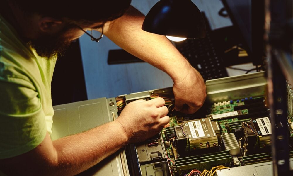 Man repairing a computer server under a lamp.