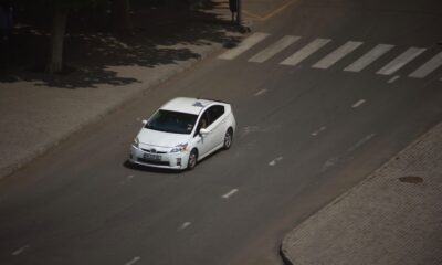 A white car driving down a street next to a tree