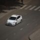 A white car driving down a street next to a tree