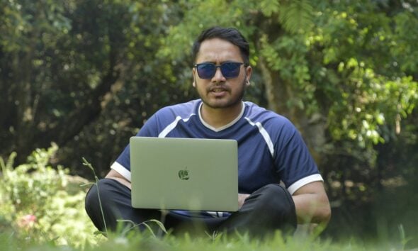 a man sitting in the grass with a laptop