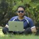 a man sitting in the grass with a laptop