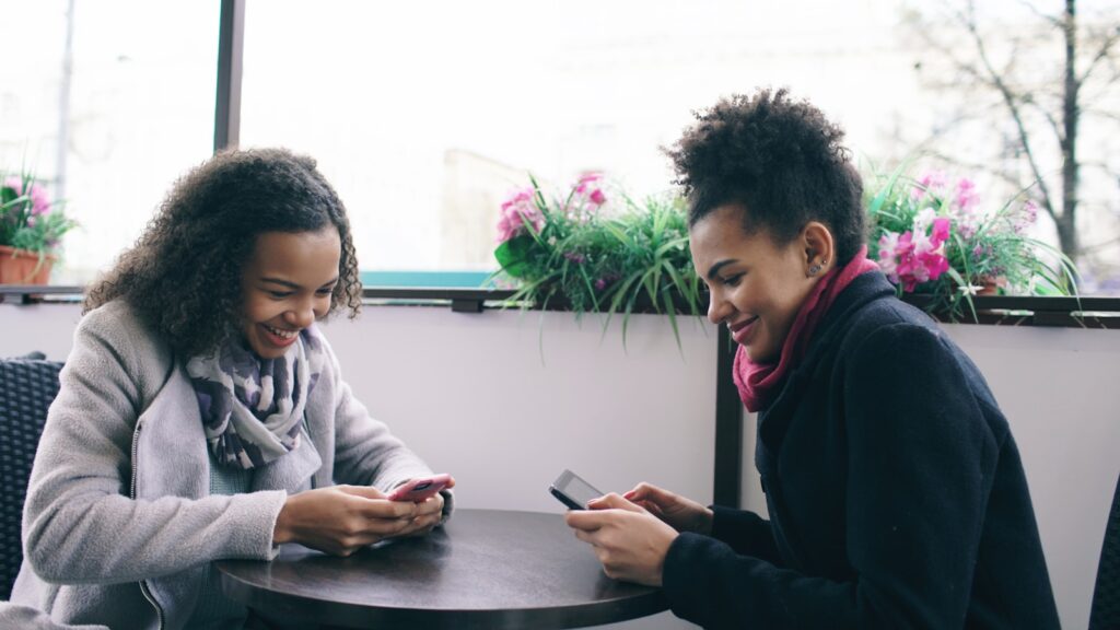 Two women laughing while looking at their phones.