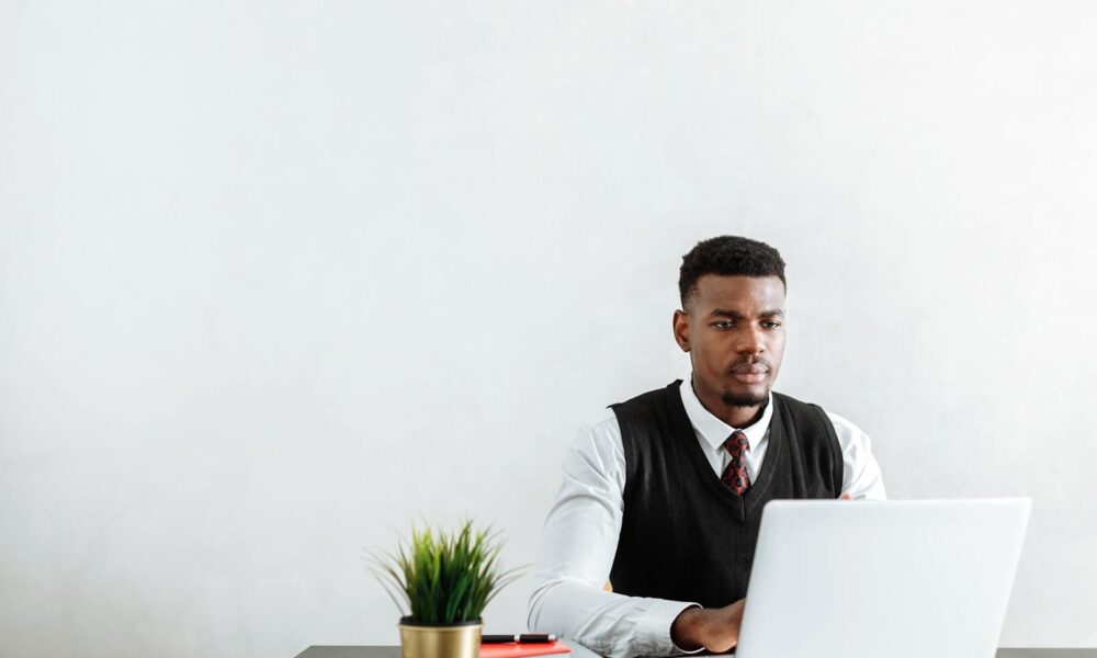 Professional man sitting at a desk working on a laptop in a modern office environment.