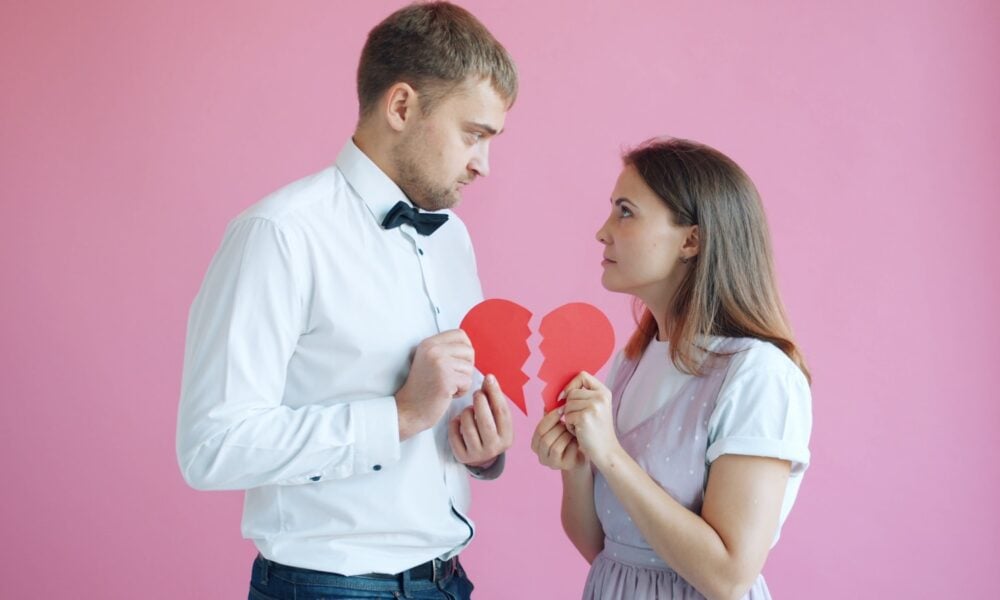 Couple holding broken heart halves on pink background