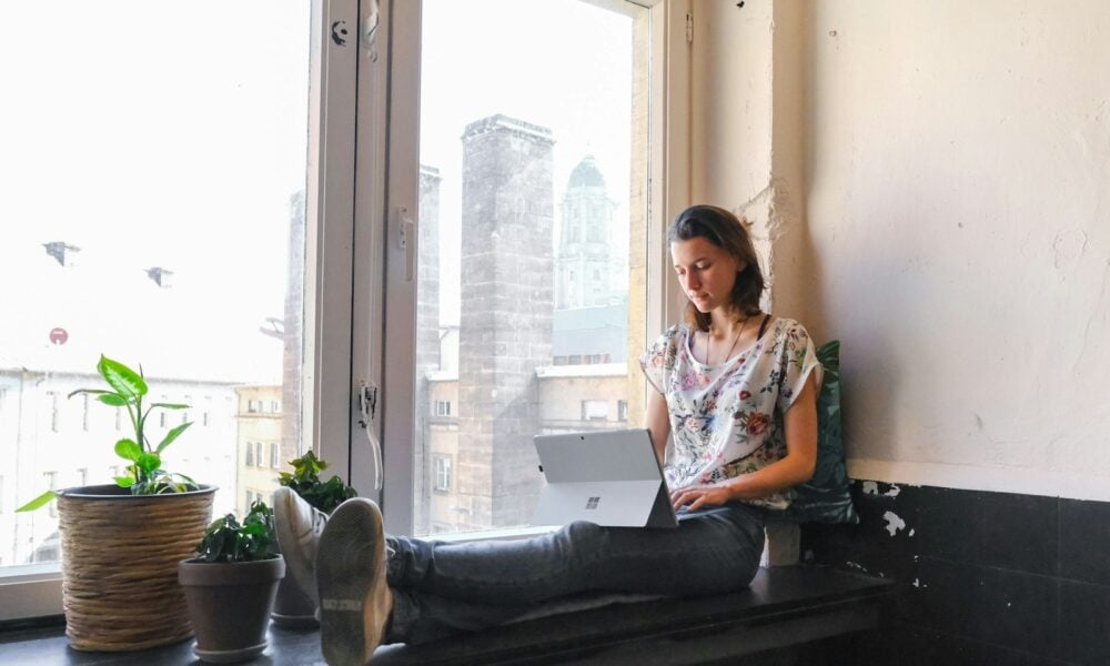 woman wearing white and red floral top sitting besides window