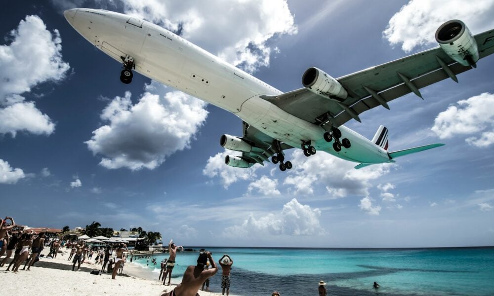 white airplane passing the people at the beach during daytime