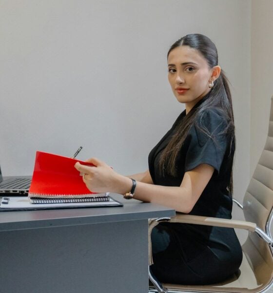 Woman working at desk with laptop and red folder.