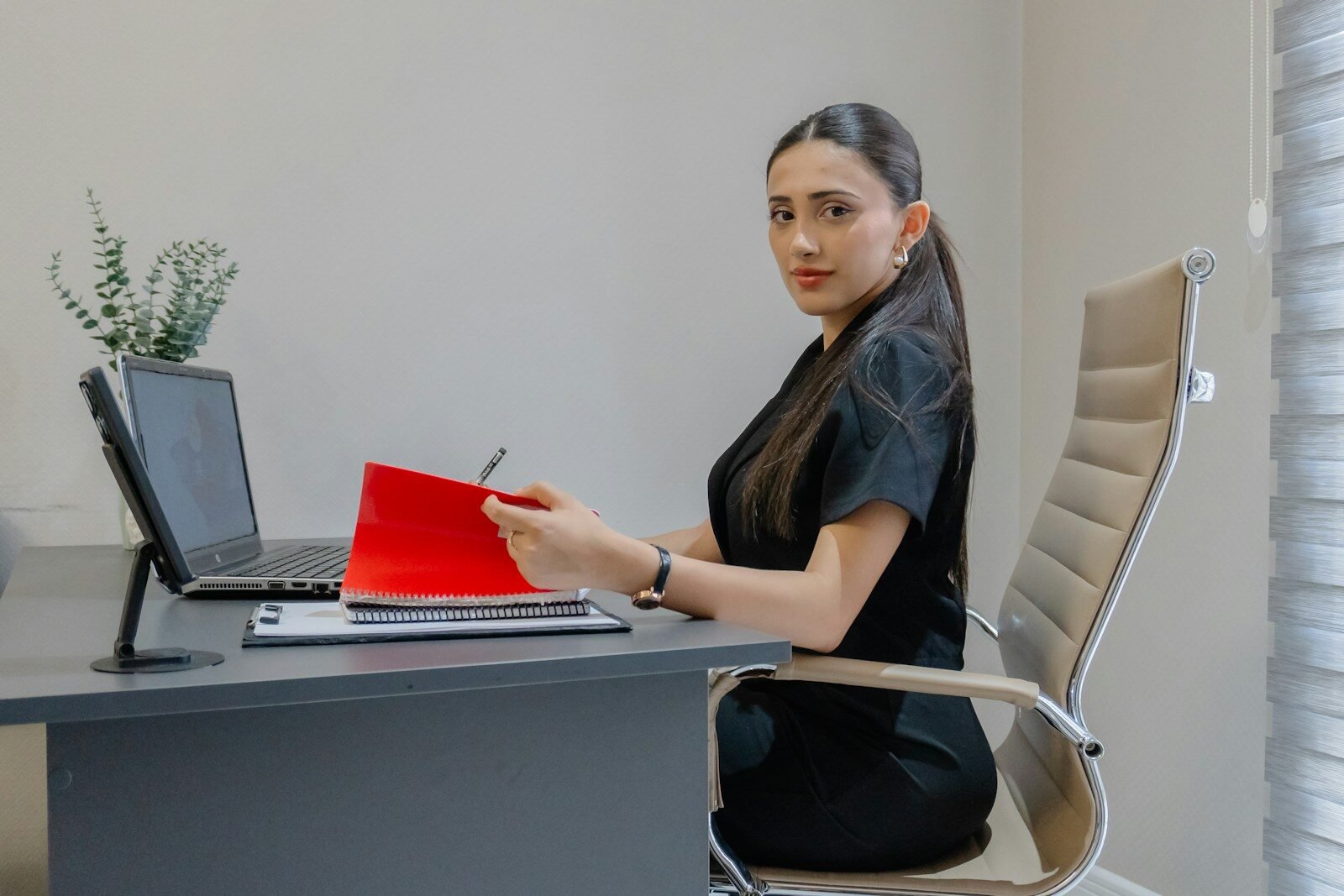 Woman working at desk with laptop and red folder.