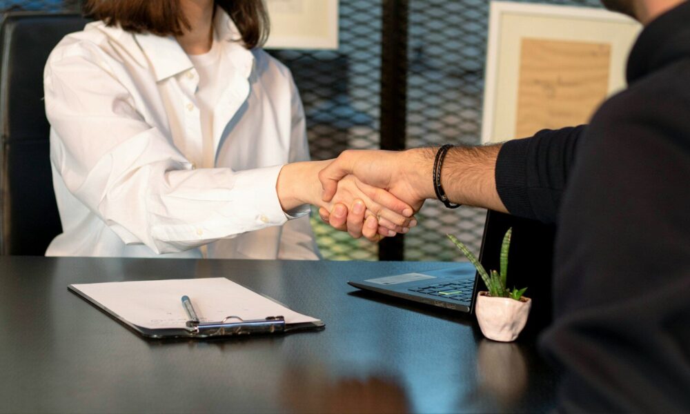 a man and a woman shaking hands in front of a laptop