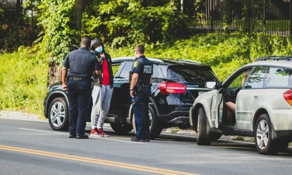 man in black t-shirt and black pants standing beside black suv during daytime
