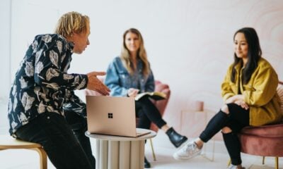 man in black and white floral long sleeve shirt sitting and showing something on a microsoft laptop to 2 women
