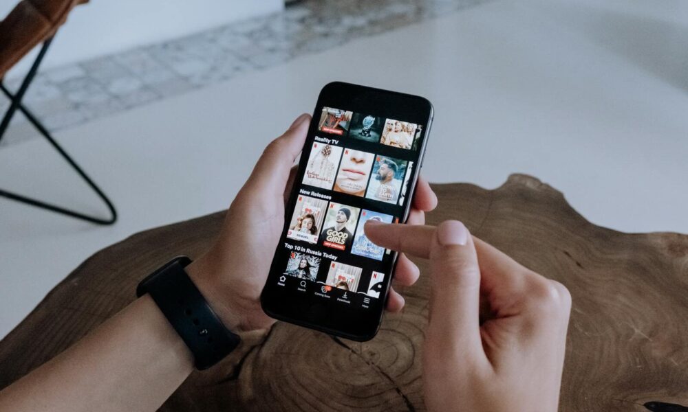 A person using a smartphone to explore and select shows on a streaming platform indoors.