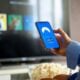 Person using VPN on smartphone while watching smart TV at home.
