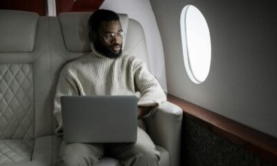 A man wearing headphones uses a laptop in a luxurious airplane cabin.