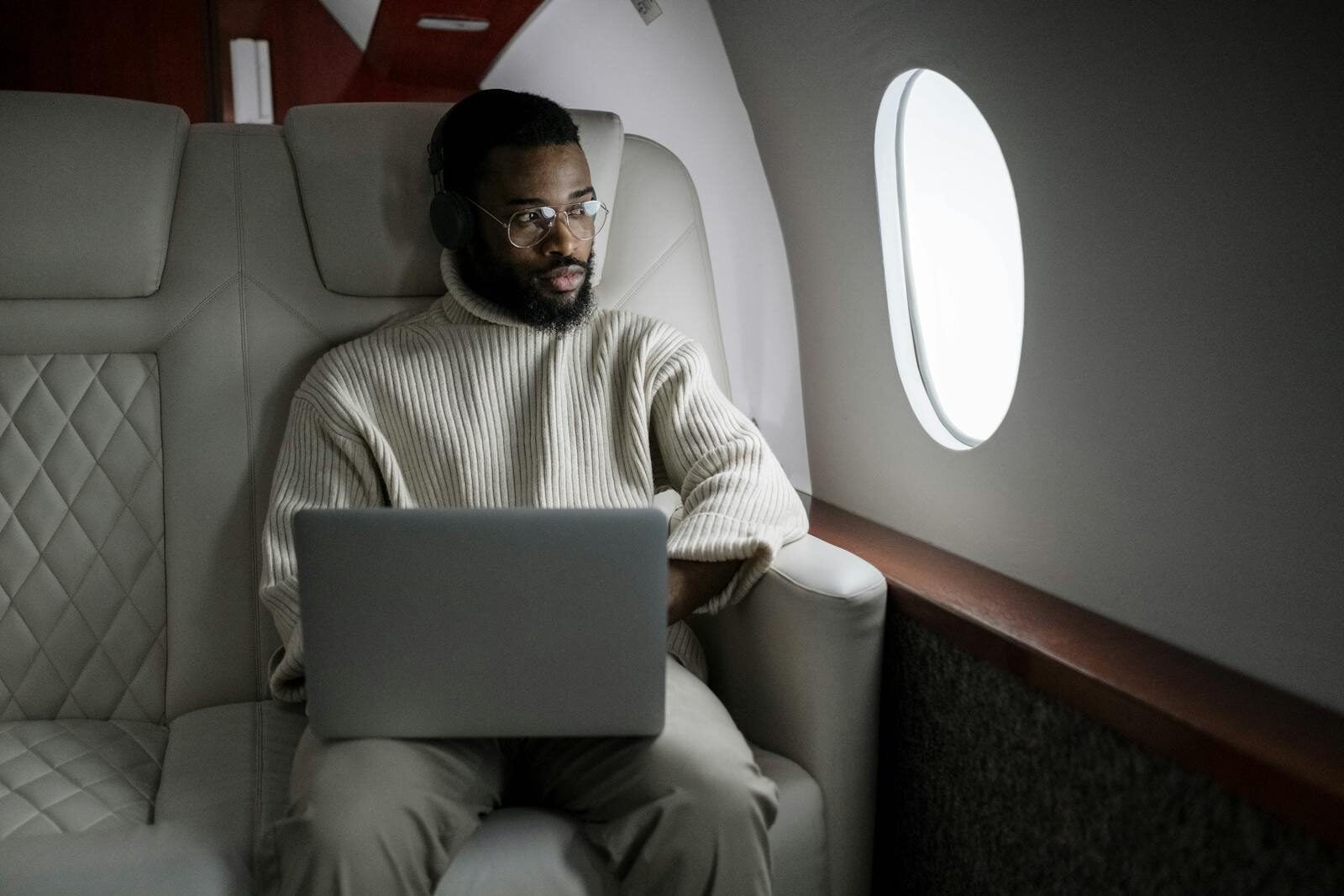 A man wearing headphones uses a laptop in a luxurious airplane cabin.