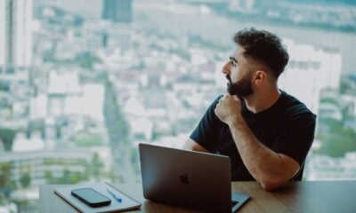 Man looking out window with laptop on desk.