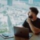 Man looking out window with laptop on desk.