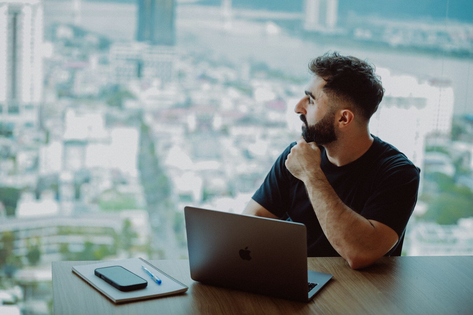 Man looking out window with laptop on desk.