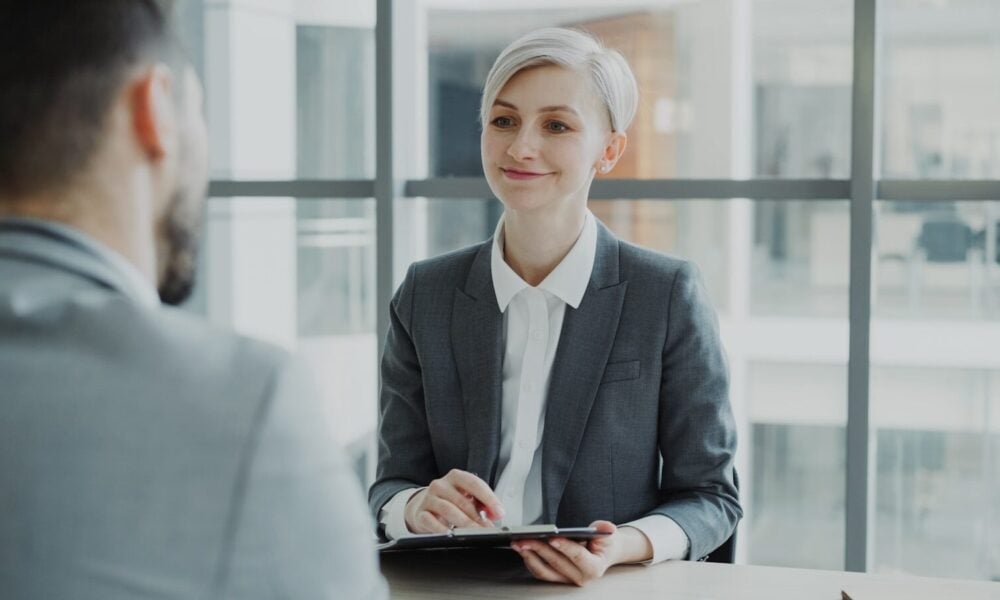 Woman in suit interviews man across table.