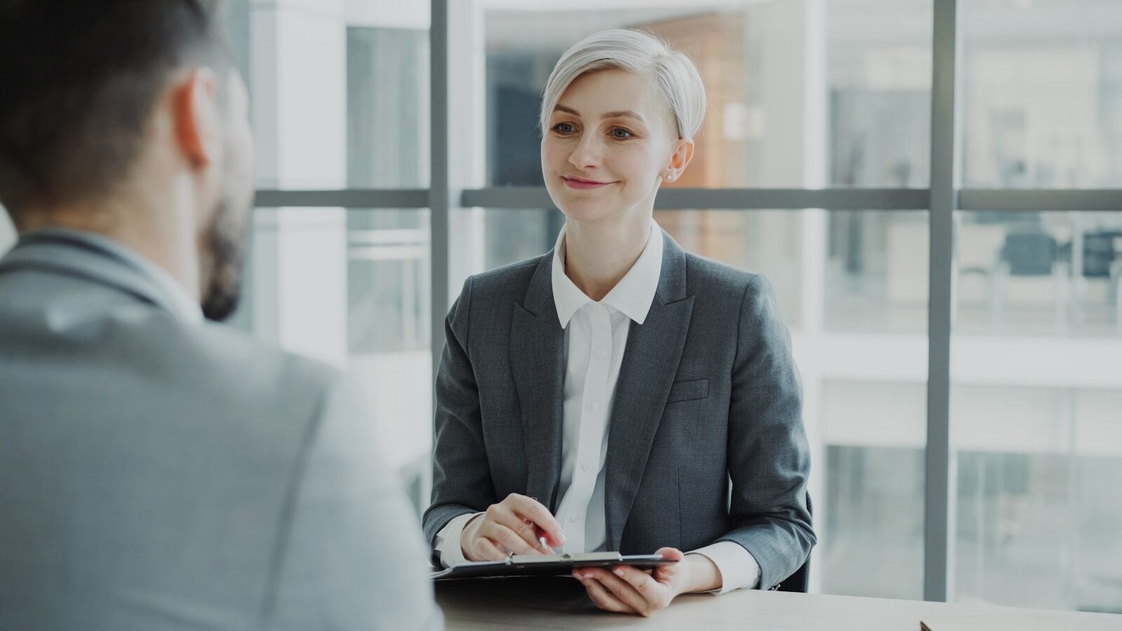 Woman in suit interviews man across table.