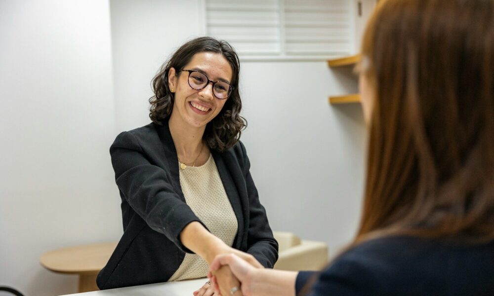 a woman shaking hands with another woman sitting at a table