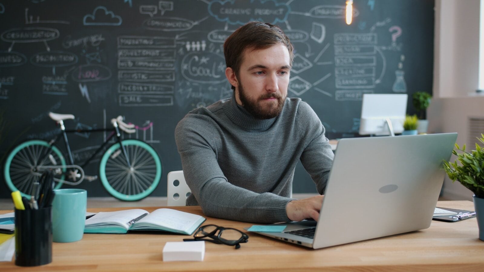 Man working on laptop in office with bicycle.